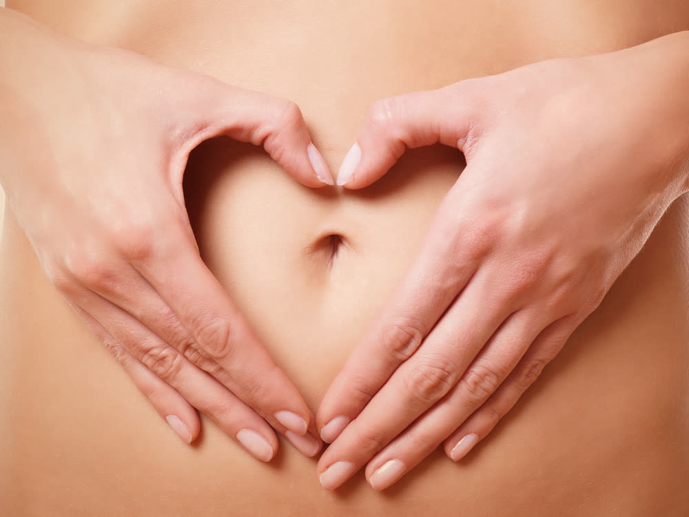Frau legt ihre Hände in Herzform auf den eigenen Bauch – Sinnbild der täglichen Selbstmassage