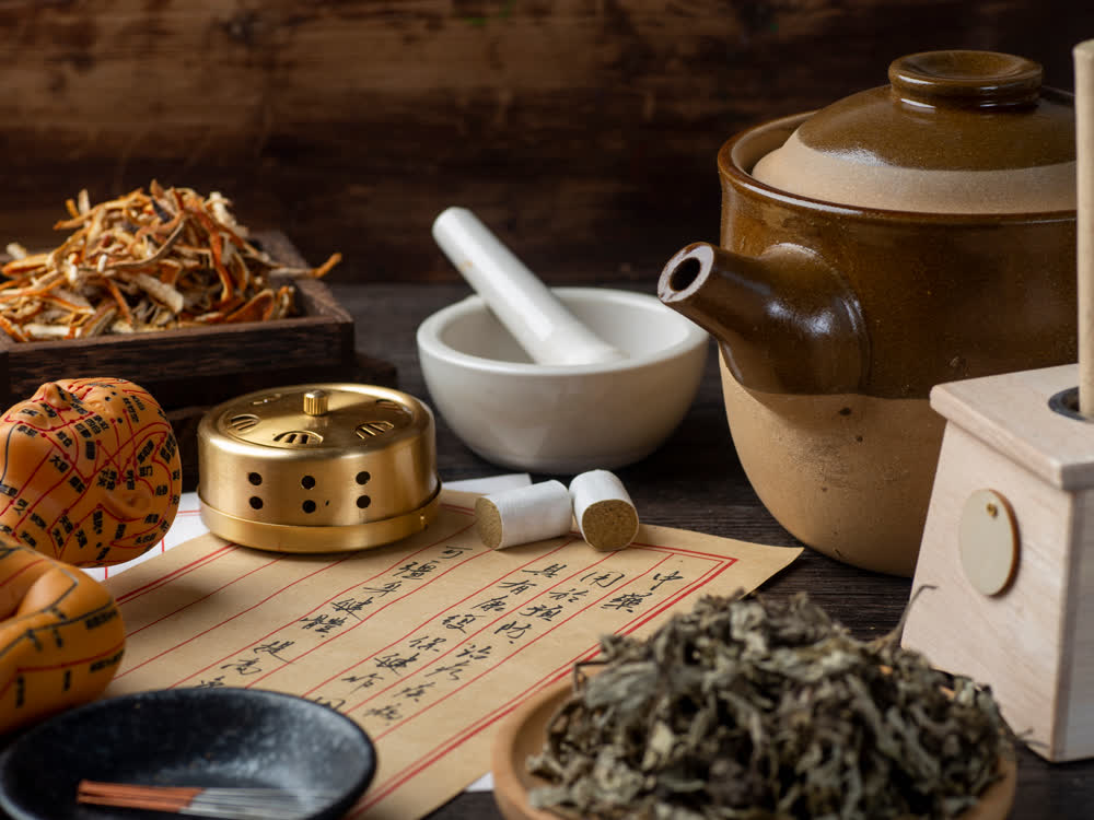 Traditionelle Chinesische Medizin – Kräuter, Reibschale, Dekoktiertopf, Moxa, Akupunkturnadeln und ein Akupunkturmodell